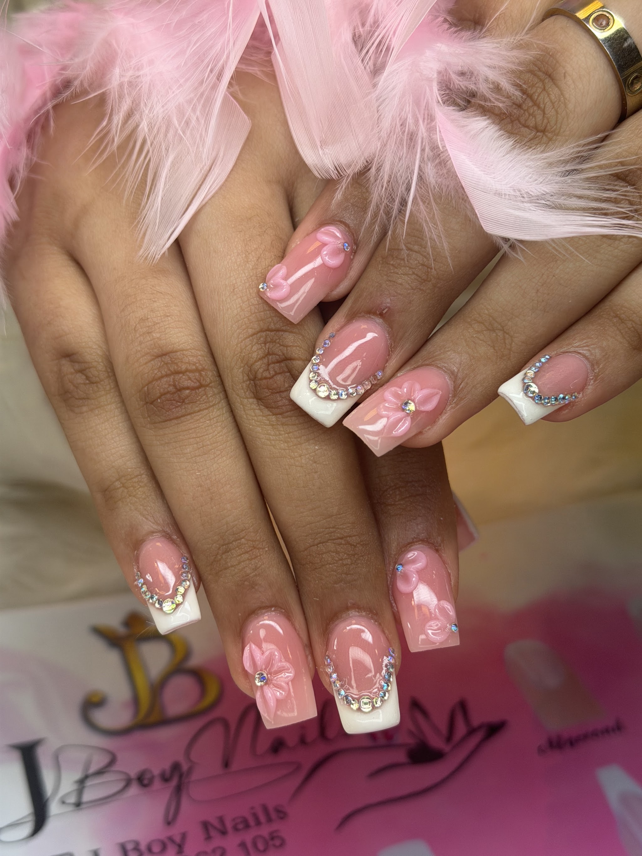Roze nagels met witte french en steentjes, naast een roze veer