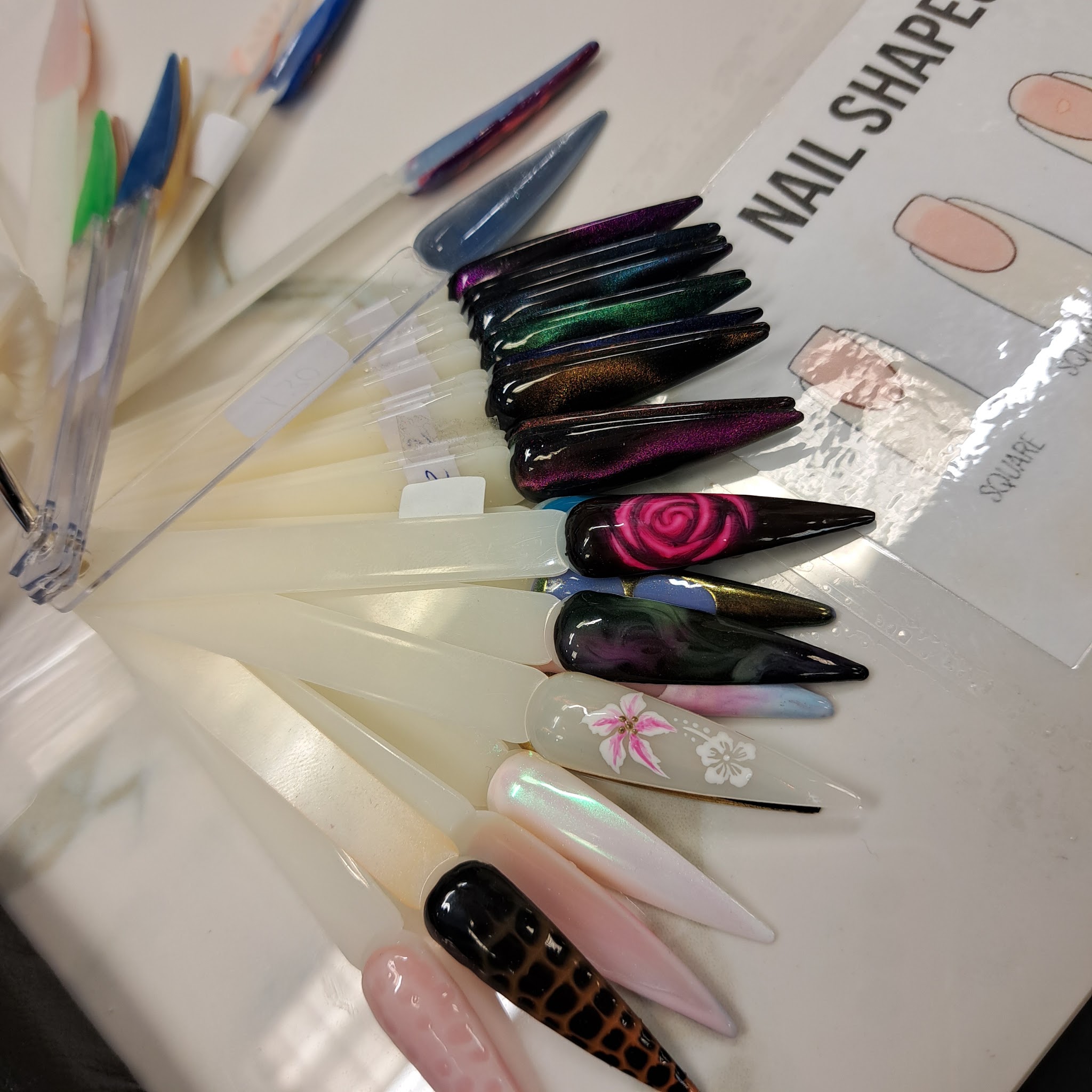 Waaier van proeftips met cat eye en geschilderde bloemen naast een kaart met nagelvormen