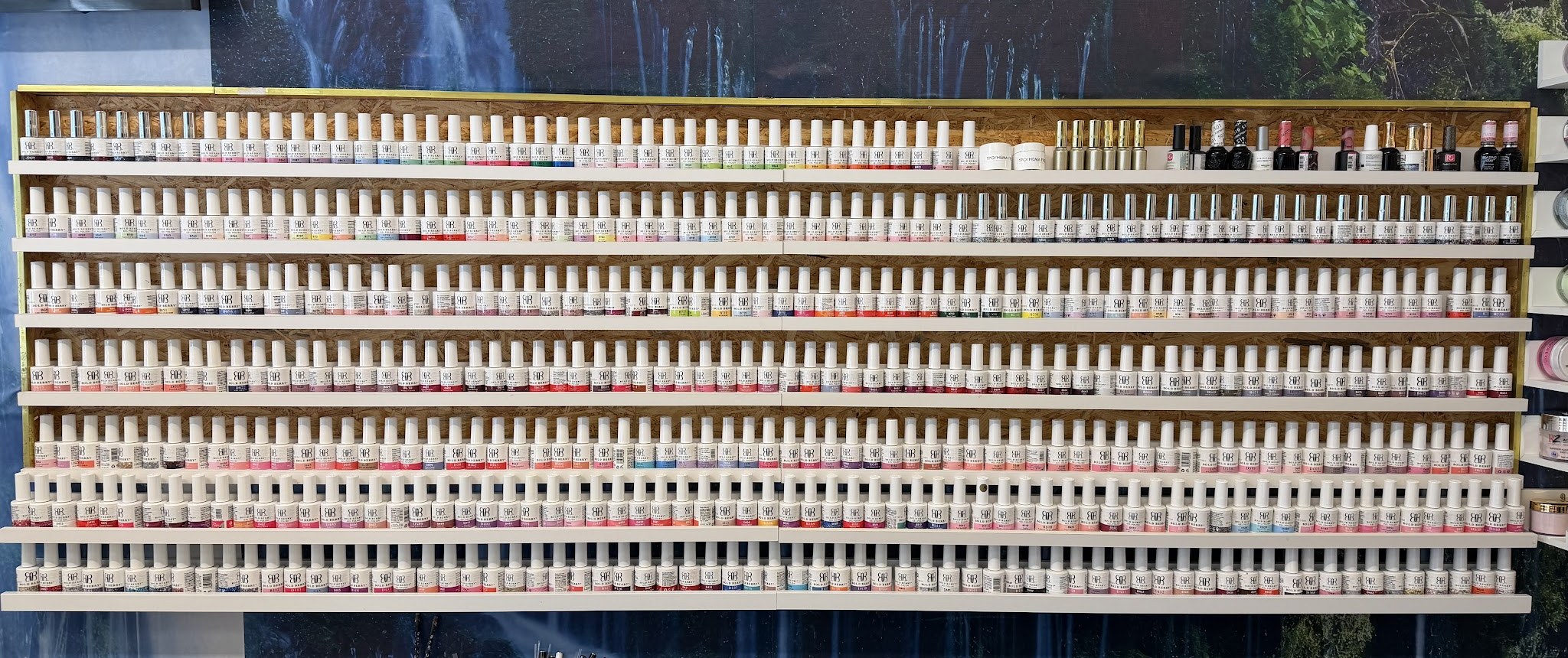 De kleurenwand in de studio: zeven planken vol flesjes gellak voor een fotobehang met een waterval